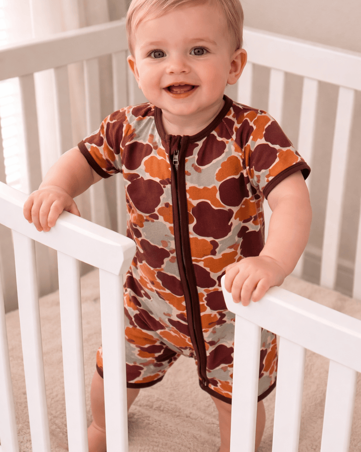 Baby in a patterned onesie standing in a crib