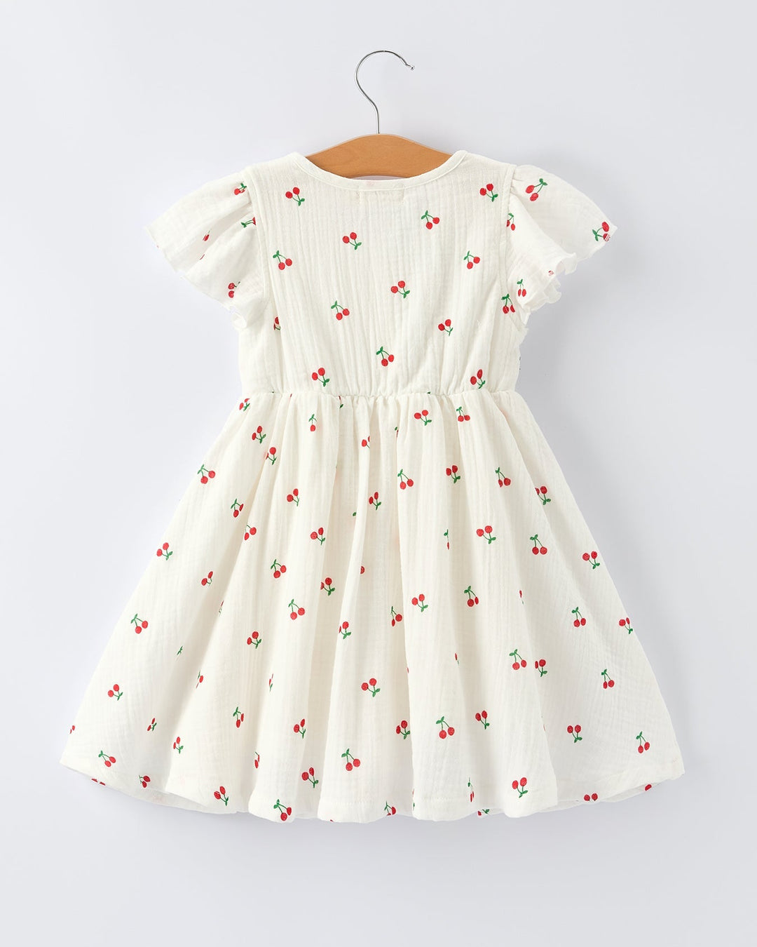 White dress with red cherry pattern on a hanger against a white background
