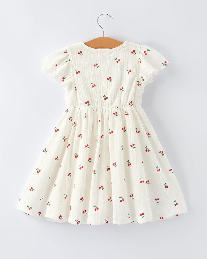 White dress with red cherry pattern on a hanger against a white background