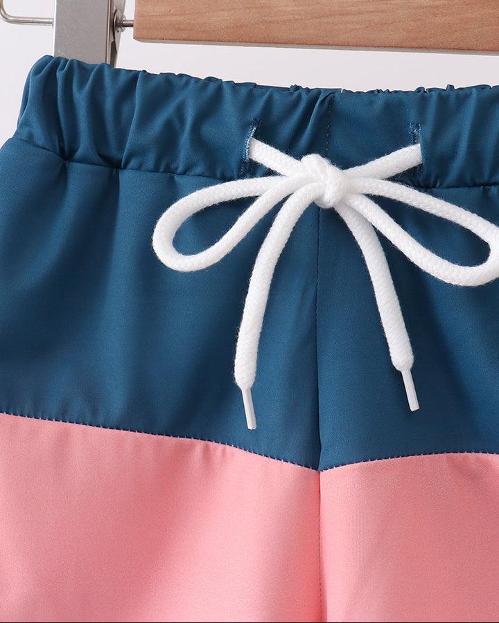 Color-blocked shorts with a white drawstring on a wooden hanger against a white background
