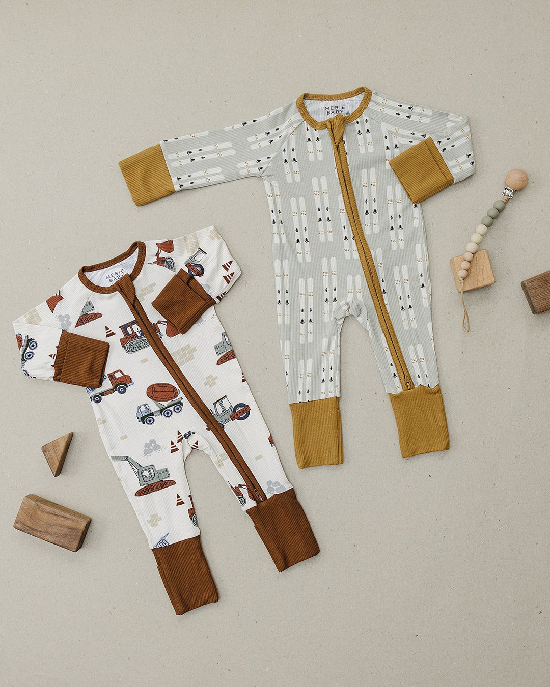 Two baby rompers with brown accents on a neutral background