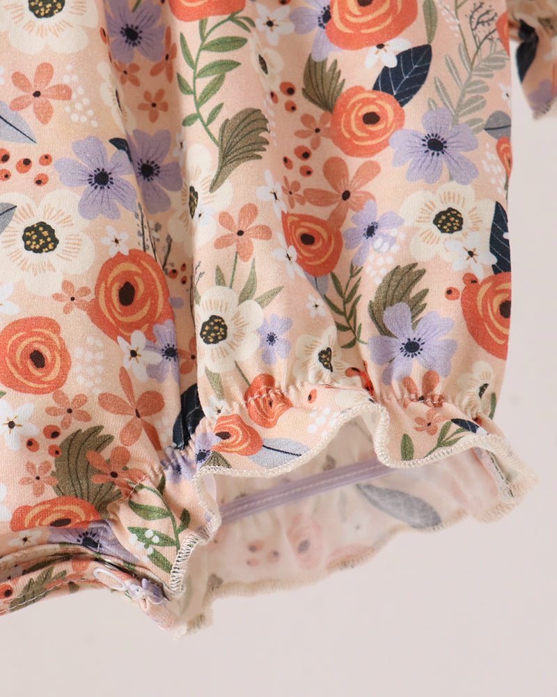 Close-up of a floral-patterned fabric garment, likely a skirt or dress, featuring orange, purple, and green flowers on a light beige background with a ruffled hem.