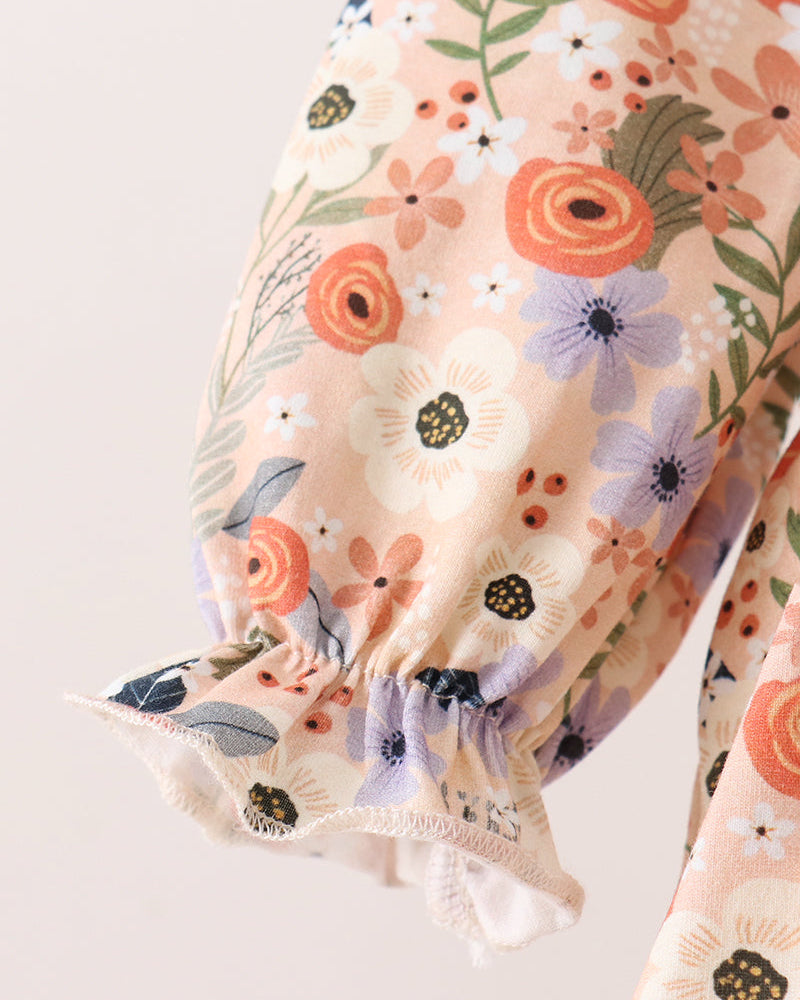 Close-up of a floral-patterned blouse sleeve with gathered elastic cuffs, featuring orange, white, and purple flowers on a light peach background.