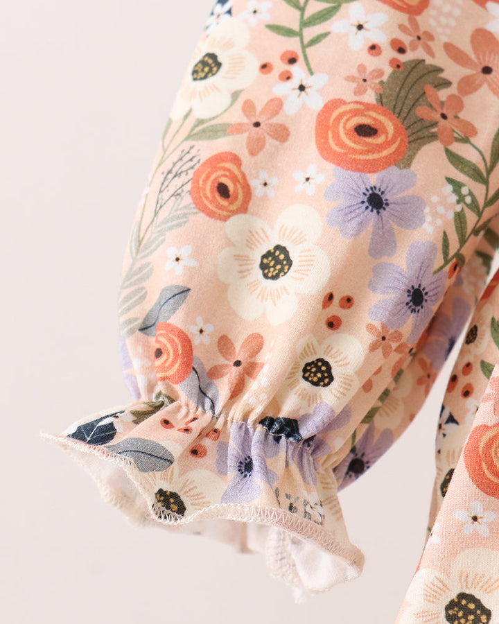 Close-up of a floral-patterned blouse sleeve with gathered elastic cuffs, featuring orange, white, and purple flowers on a light peach background.