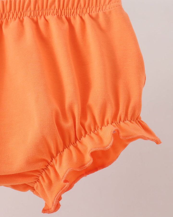Close-up of bright orange bloomers with an elastic waistband and ruffled hem, shown against a plain light background.