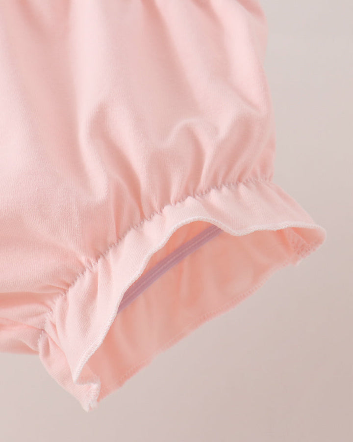 Close-up of a light pink garment with an elasticized ruffled cuff, shown against a soft light beige background.