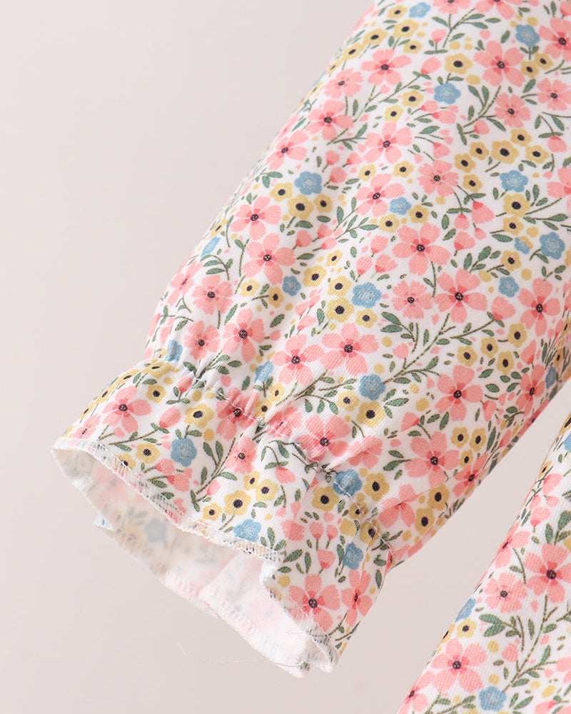 Close-up of a floral-patterned fabric garment, showing a ruffled cuff with a dense print of pink, yellow, blue, and green flowers on a light background.