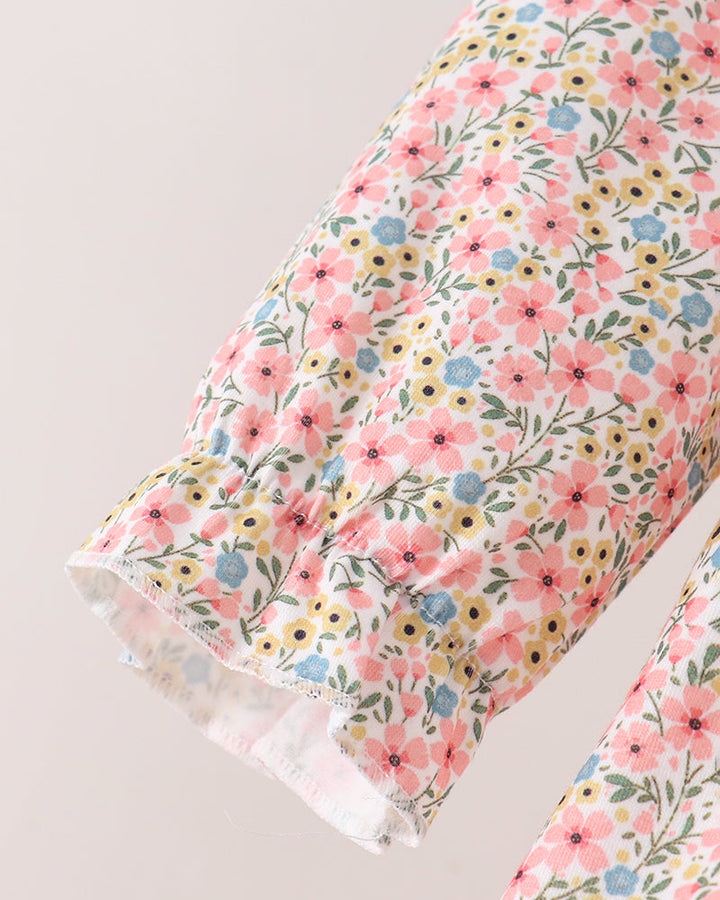 Close-up of a floral-patterned fabric garment, showing a ruffled cuff with a dense print of pink, yellow, blue, and green flowers on a light background.