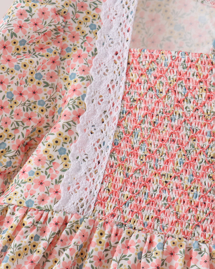 Close-up of a floral dress with a pink and yellow ditsy print, featuring a smocked bodice, white eyelet lace trim, and a gathered skirt.