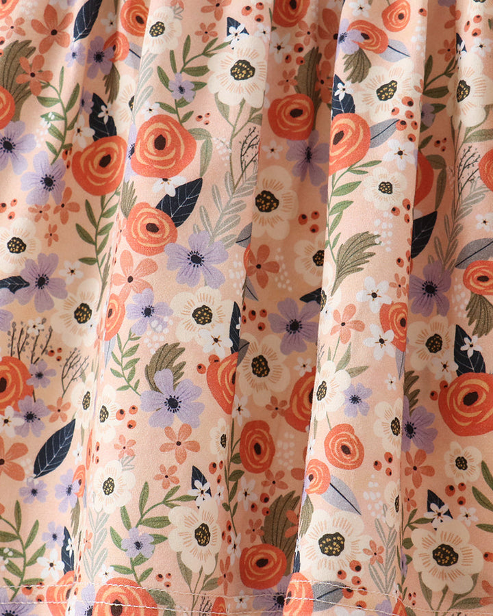 Close-up of a floral fabric with a cream background and a pattern of orange, purple, and green flowers and leaves.