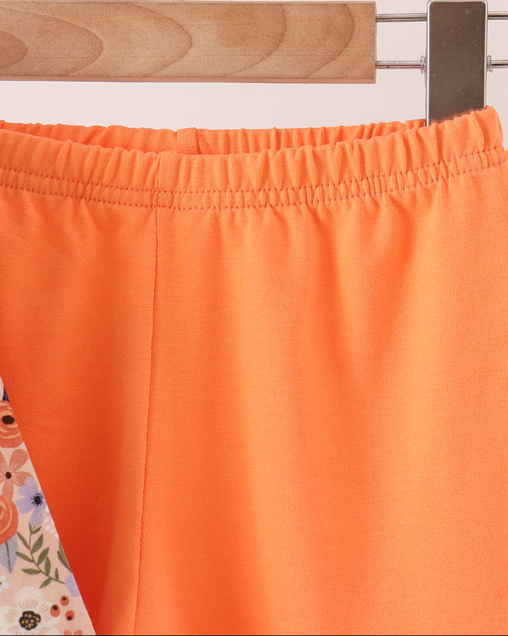 Close-up of bright orange shorts with an elastic waistband, hanging on a wooden hanger against a light background.