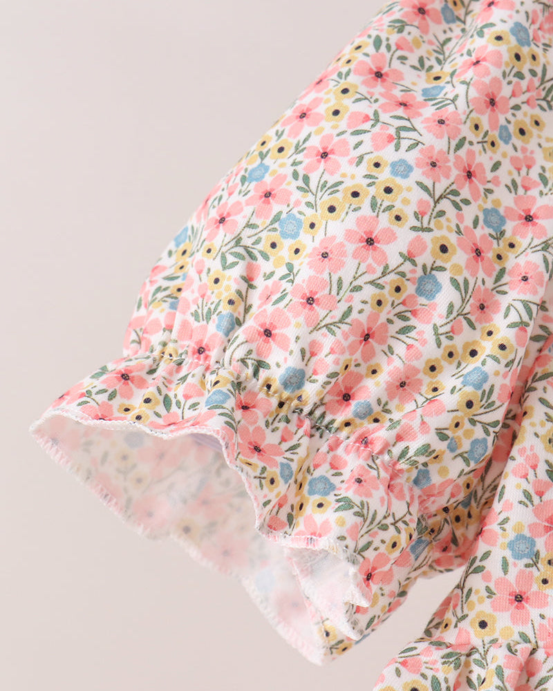 A close-up of a floral-patterned fabric garment, showing a ruffled sleeve or hem detail with pink, yellow, and blue flowers on a light background.