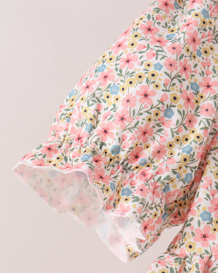 A close-up of a floral-patterned fabric garment, showing a ruffled sleeve or hem detail with pink, yellow, and blue flowers on a light background.