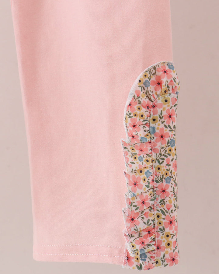 A close-up of a light pink garment, likely leggings or pants, showing a decorative floral fabric panel attached along the lower leg. The floral pattern contains pink, yellow, blue, and green tones.