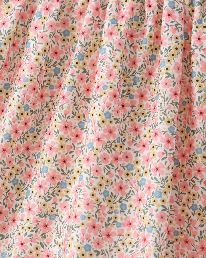 Close-up of a floral fabric with a smocked elastic waistband, featuring pink, yellow, and blue flowers with green leaves on a cream background.