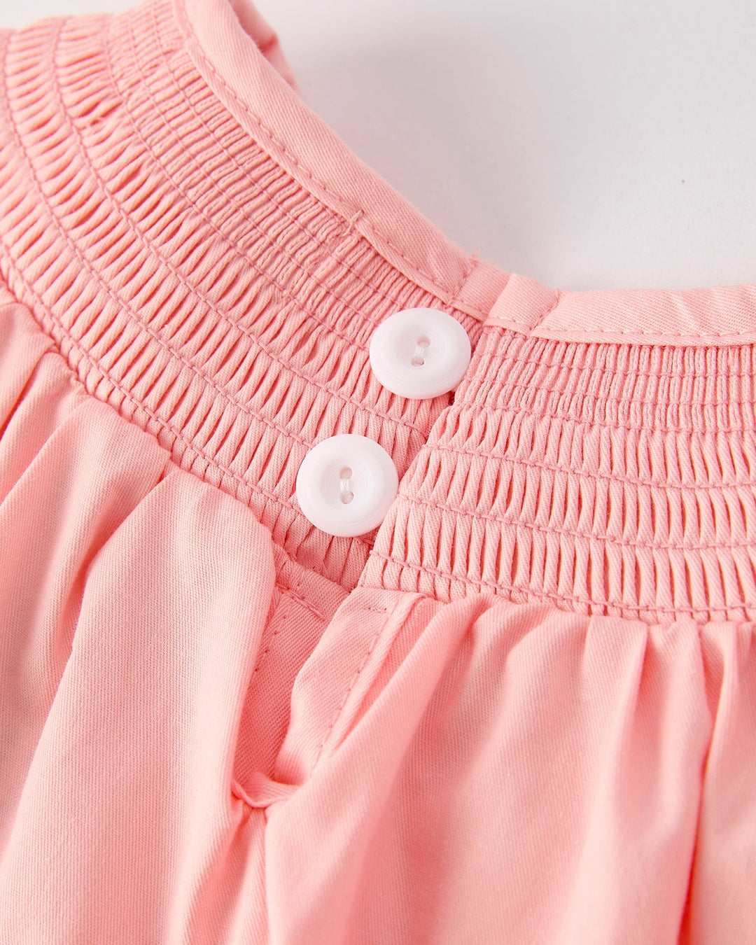 Close-up of a pink garment with smocked waistband and buttons on a white background
