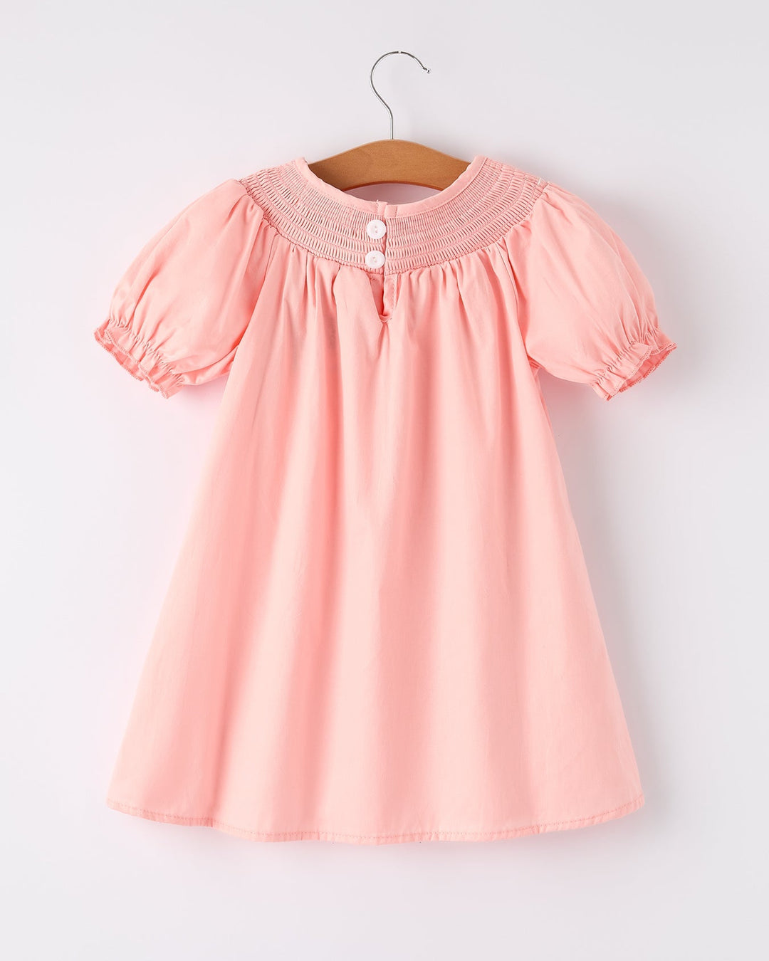 Pink dress with smocked neckline on a hanger against a white background