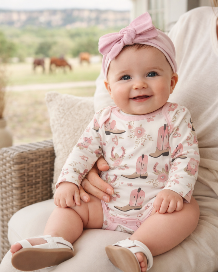Baby wearing a pink outfit with cowboy boot prints, sitting on a person&