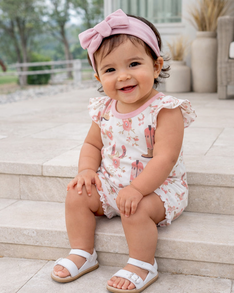 Baby sitting on steps wearing a floral romper and pink headband.
