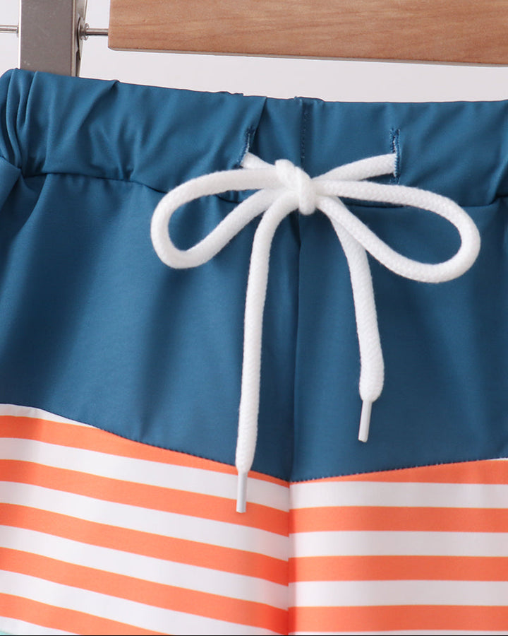 Blue and orange striped swim shorts with a white drawstring on a wooden rack.