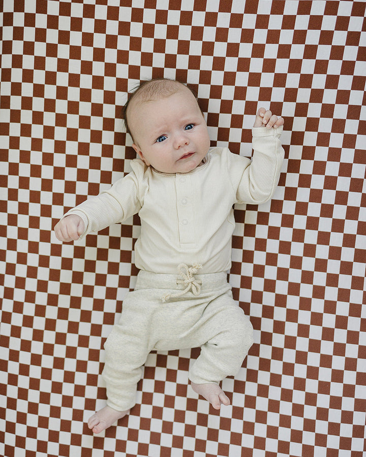 Baby in a white outfit lying on a red and white checkered floor