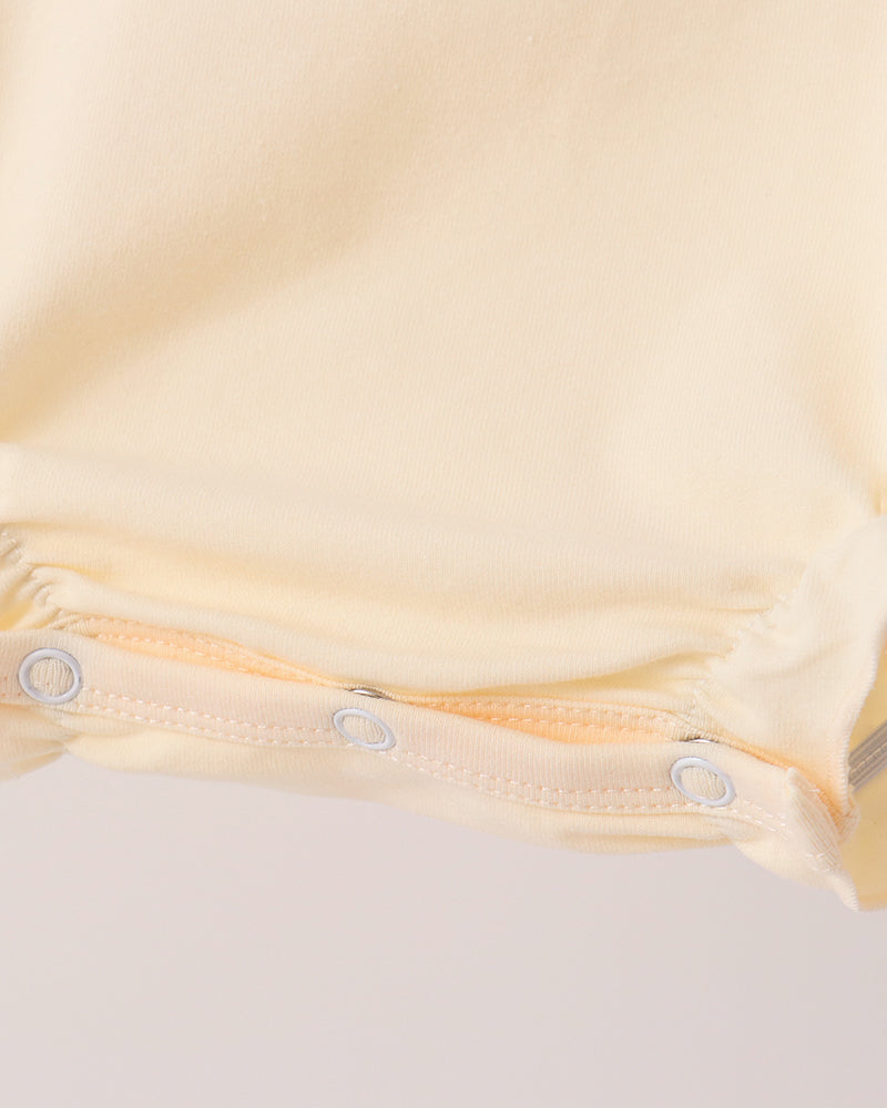 Cream romper leg opening with snap buttons along the edge, close-up