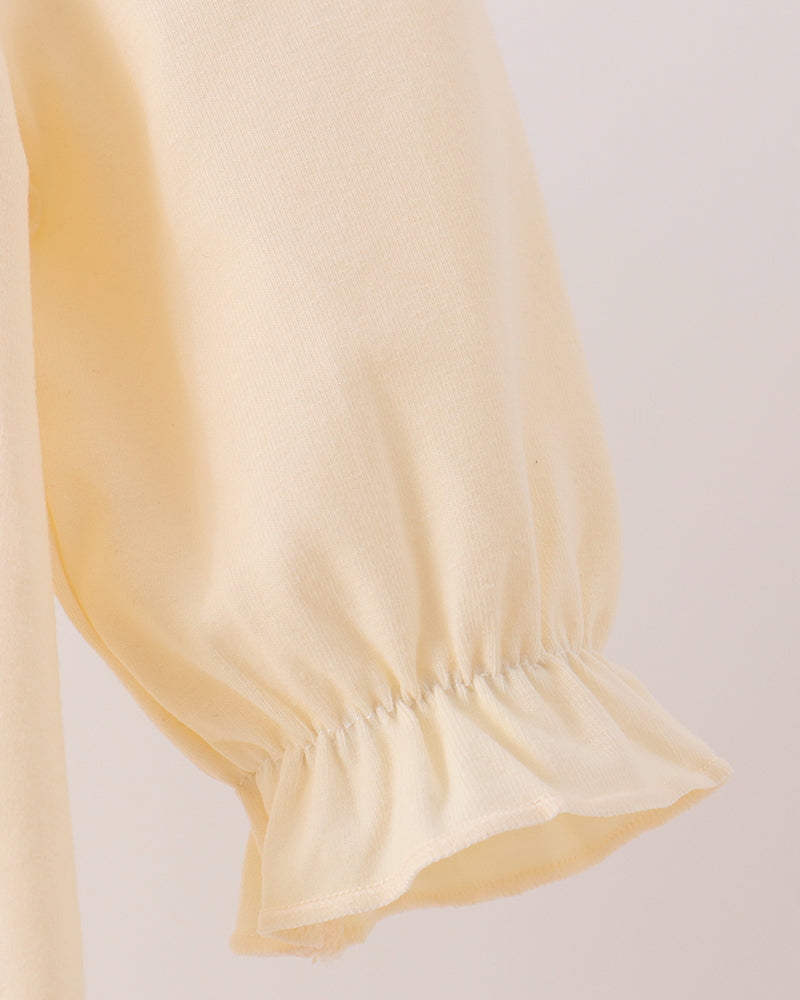 Cream long sleeve with gathered cuff and soft ruffle hem, close-up