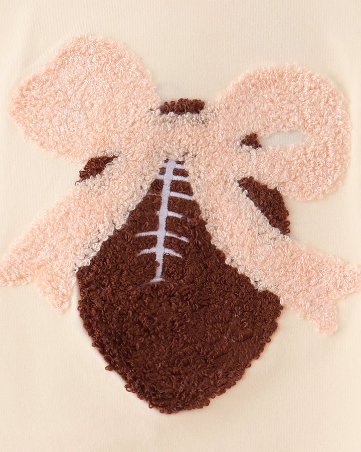 Cream dress with fuzzy football-style applique, brown center, and pink bow