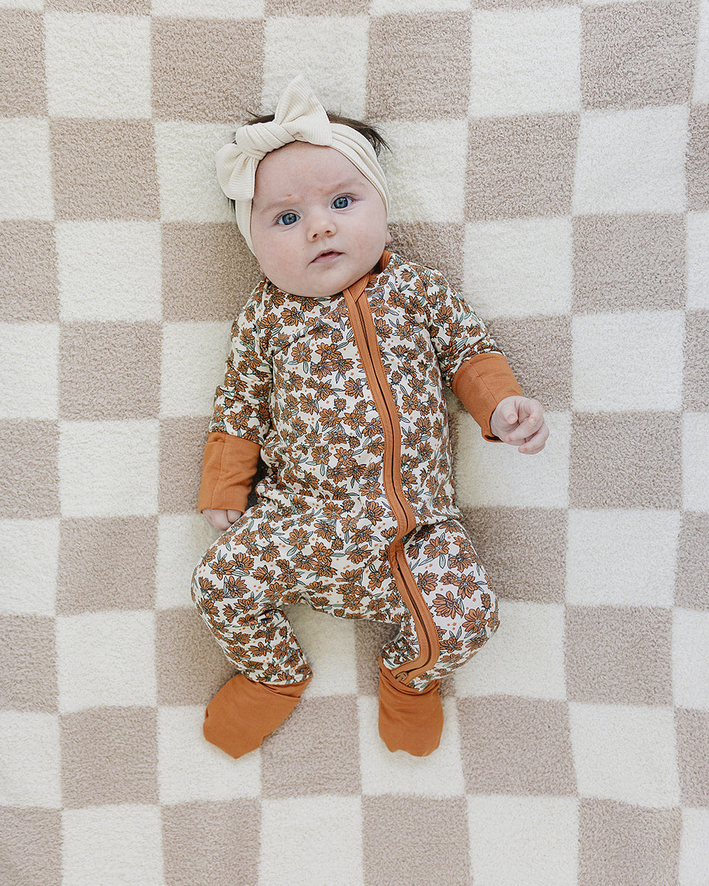 Baby in a patterned onesie with orange accents lying on a checkered blanket