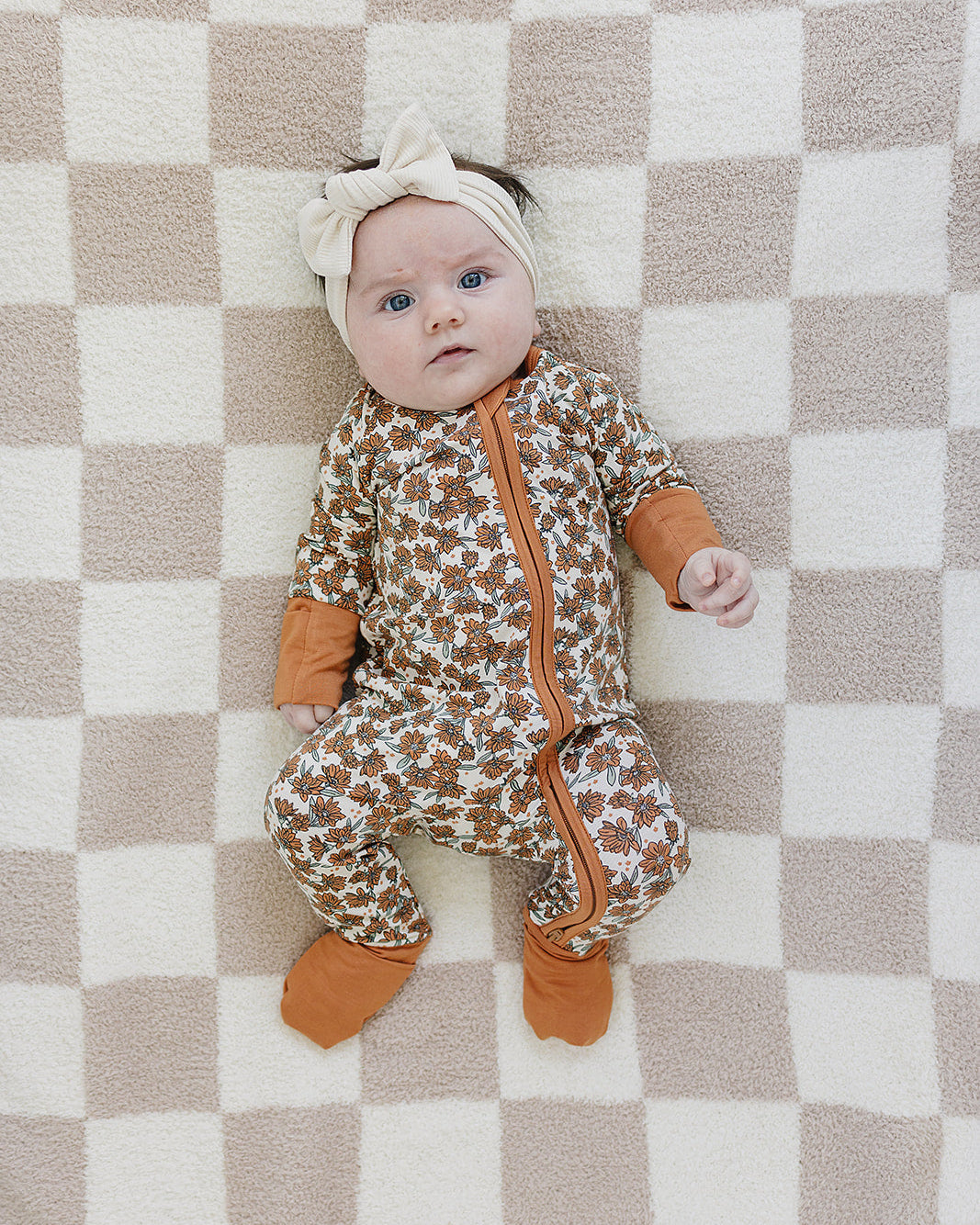 Baby in a patterned onesie with orange accents lying on a checkered blanket