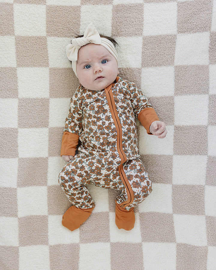 Baby in a patterned onesie with orange accents lying on a checkered blanket