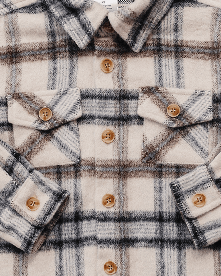 Close-up of a plaid flannel shirt in cream, brown, and gray, featuring brown wooden buttons and two chest flap pockets.