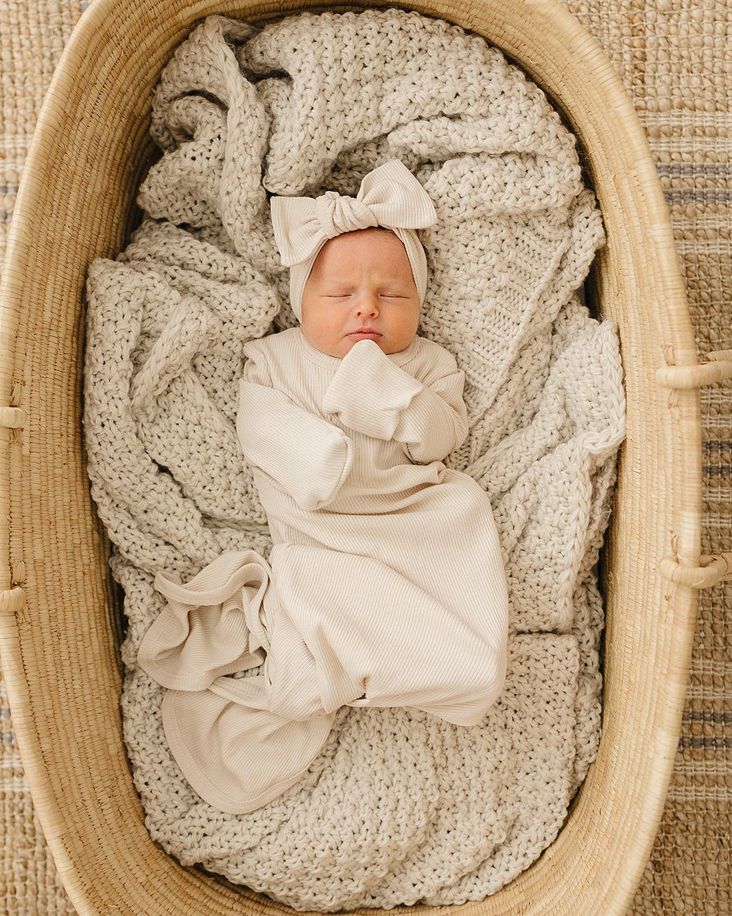 Newborn baby wrapped in a beige blanket with a bow, lying in a woven basket.