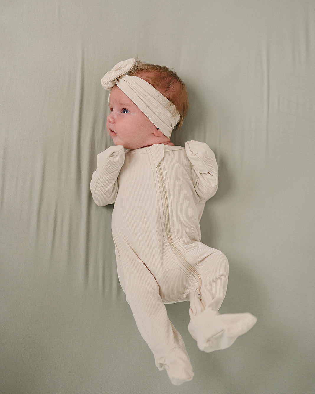 Baby in a white onesie and headband against a plain background