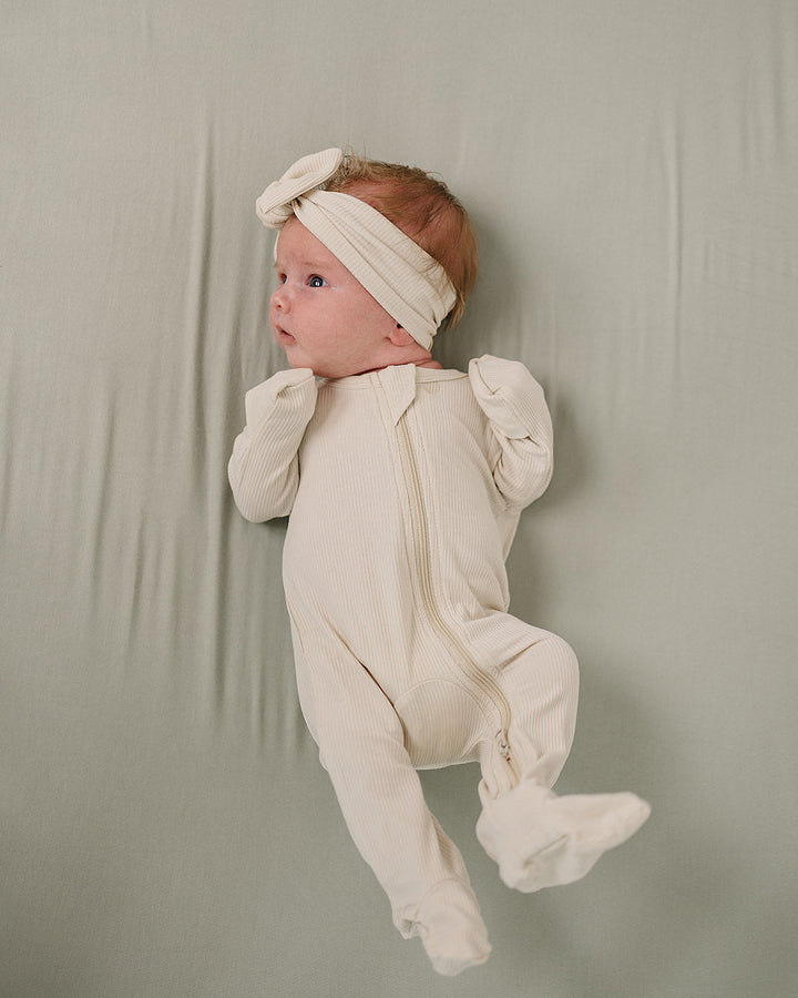 Baby in a white onesie and headband against a plain background