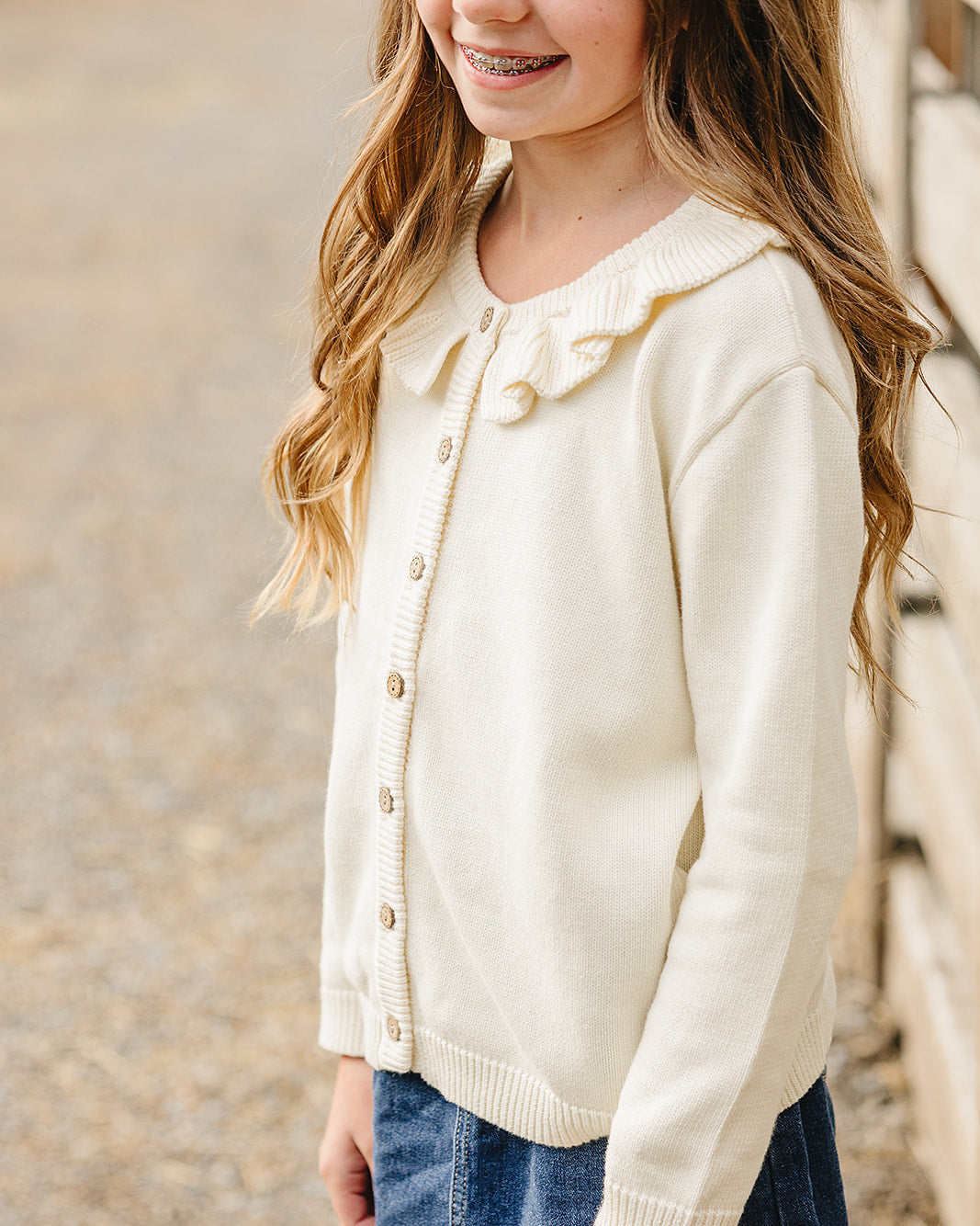 Cream knit ruffle cardigan with button front, long sleeves, and scalloped neckline trim