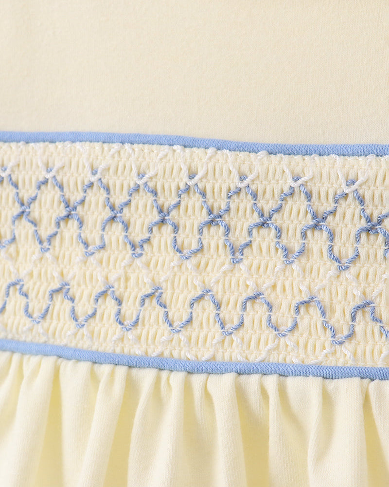 Close-up of cream smocked bodice with blue embroidered trim and gathered waist