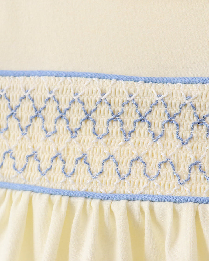 Close-up of cream smocked bodice with blue embroidered trim and gathered waist