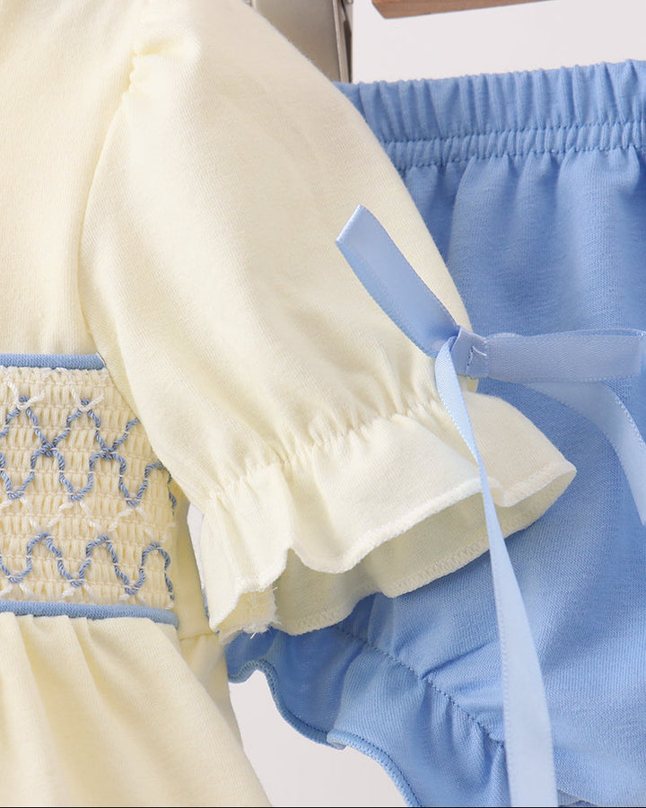 Cream dress and blue bloomer set on hangers, with bow ties and puff sleeves