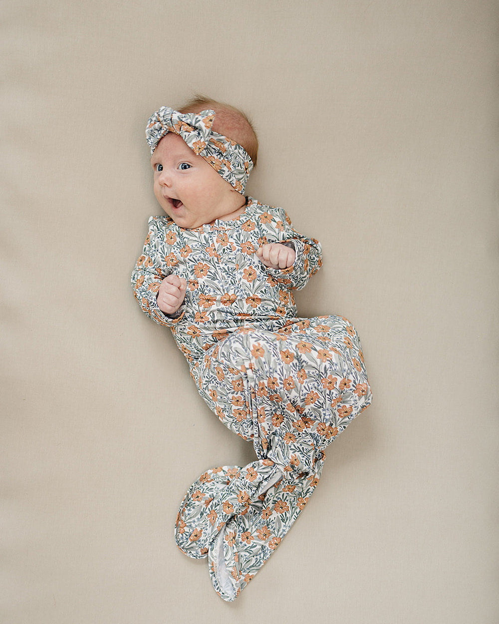 Baby wrapped in a floral blanket with a matching headband on a beige background