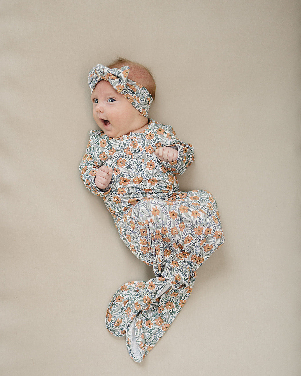 Baby wrapped in a floral blanket with a matching headband on a beige background
