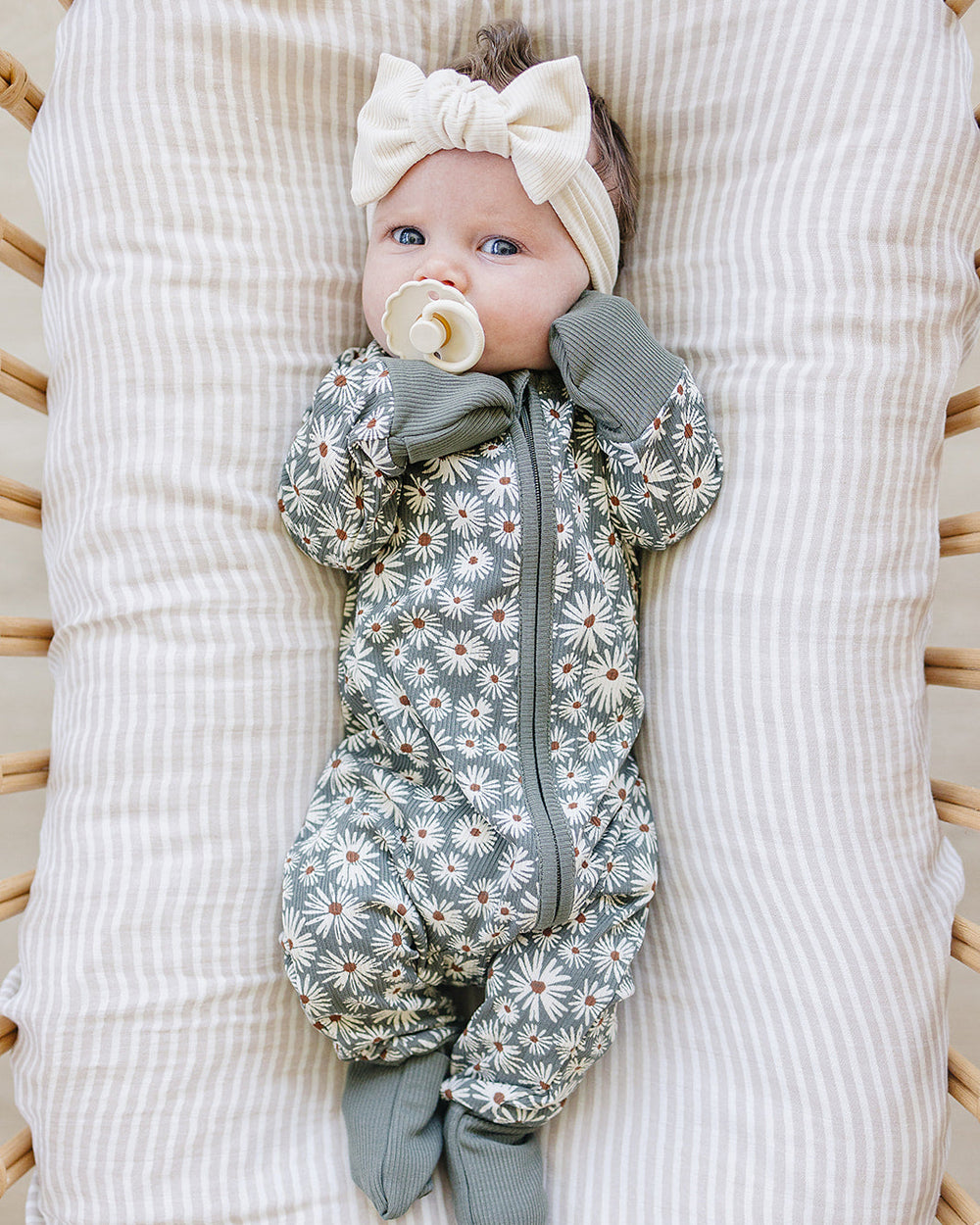 Baby lying on a textured white blanket wearing a floral onesie and headband.