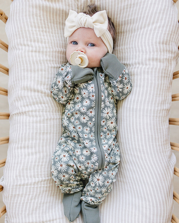 Baby lying on a textured white blanket wearing a floral onesie and headband.