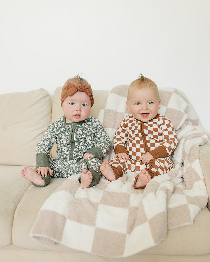 Two babies sitting on a couch with a checkered blanket
