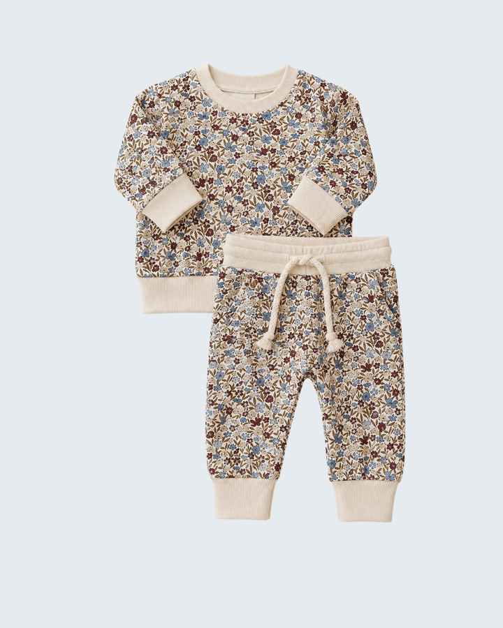 A two-piece kids clothing set featuring a long-sleeve top and matching jogger pants. The set has a dense, small-scale floral print in shades of blue, brown, and red on a warm beige background, with solid beige ribbed cuffs, collar, and hem on the top, and a matching beige drawstring waist on the pants.