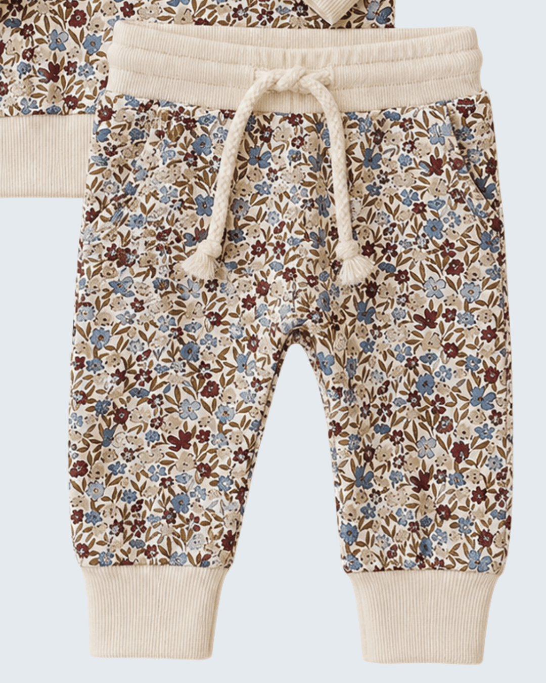 A pair of baby jogger pants featuring a dense floral print in blue, brown, and beige, with solid cream-colored ribbed cuffs and an elastic waistband with a matching cream drawstring.