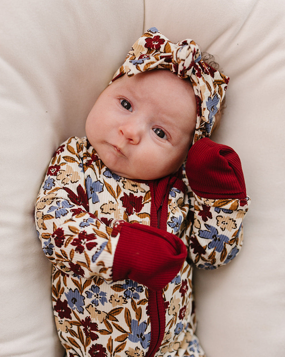 Baby in a floral outfit with red accents on a beige surface