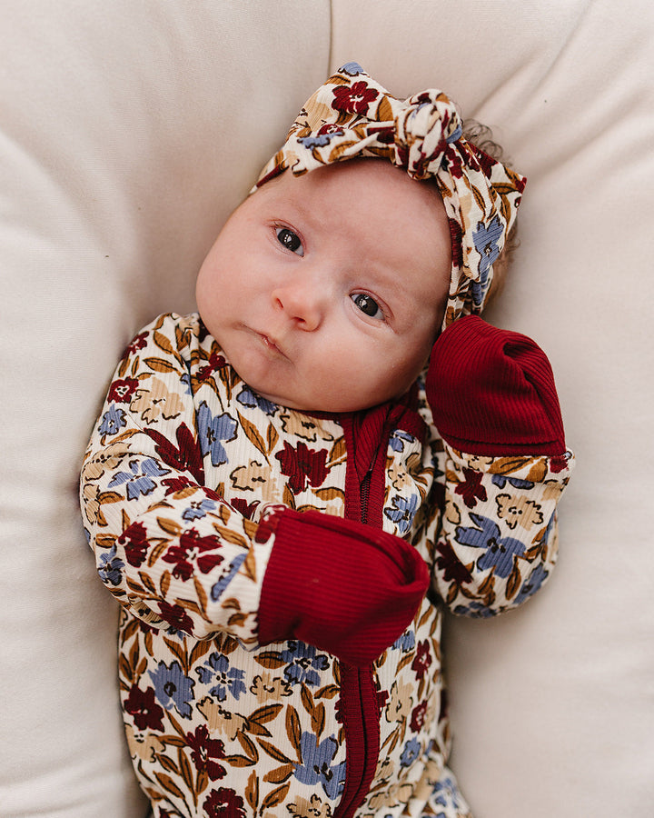 Baby in a floral outfit with red accents on a beige surface