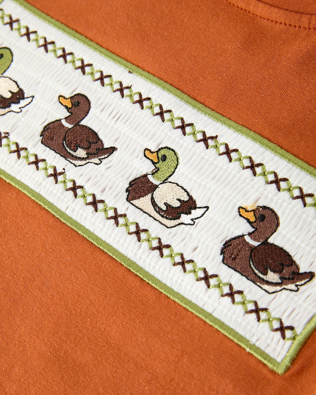 Embroidered design of ducks on a piece of fabric with an orange background