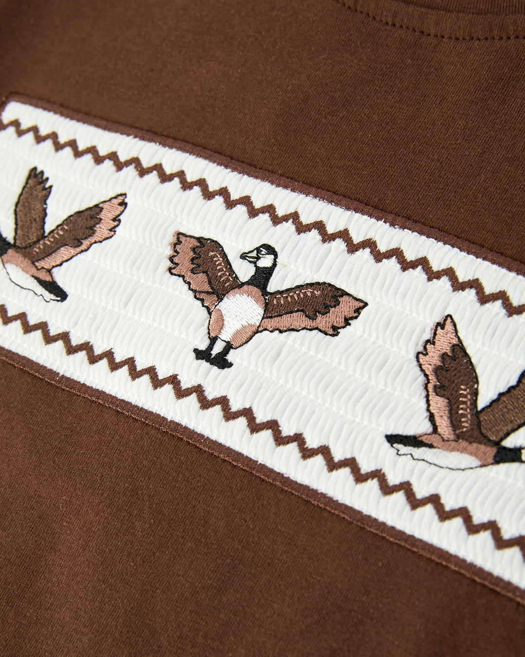 Close-up of a brown garment with embroidered geese on a white background